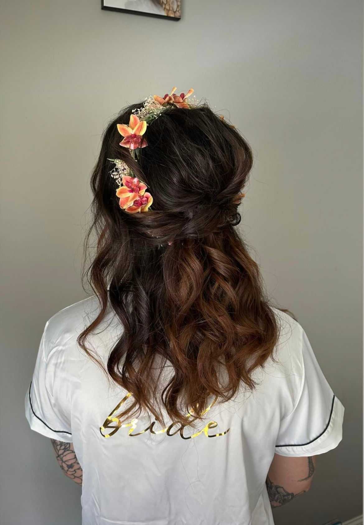 Bride with floral hair accessories and curled hair, wearing a white robe with "bride" on the back.