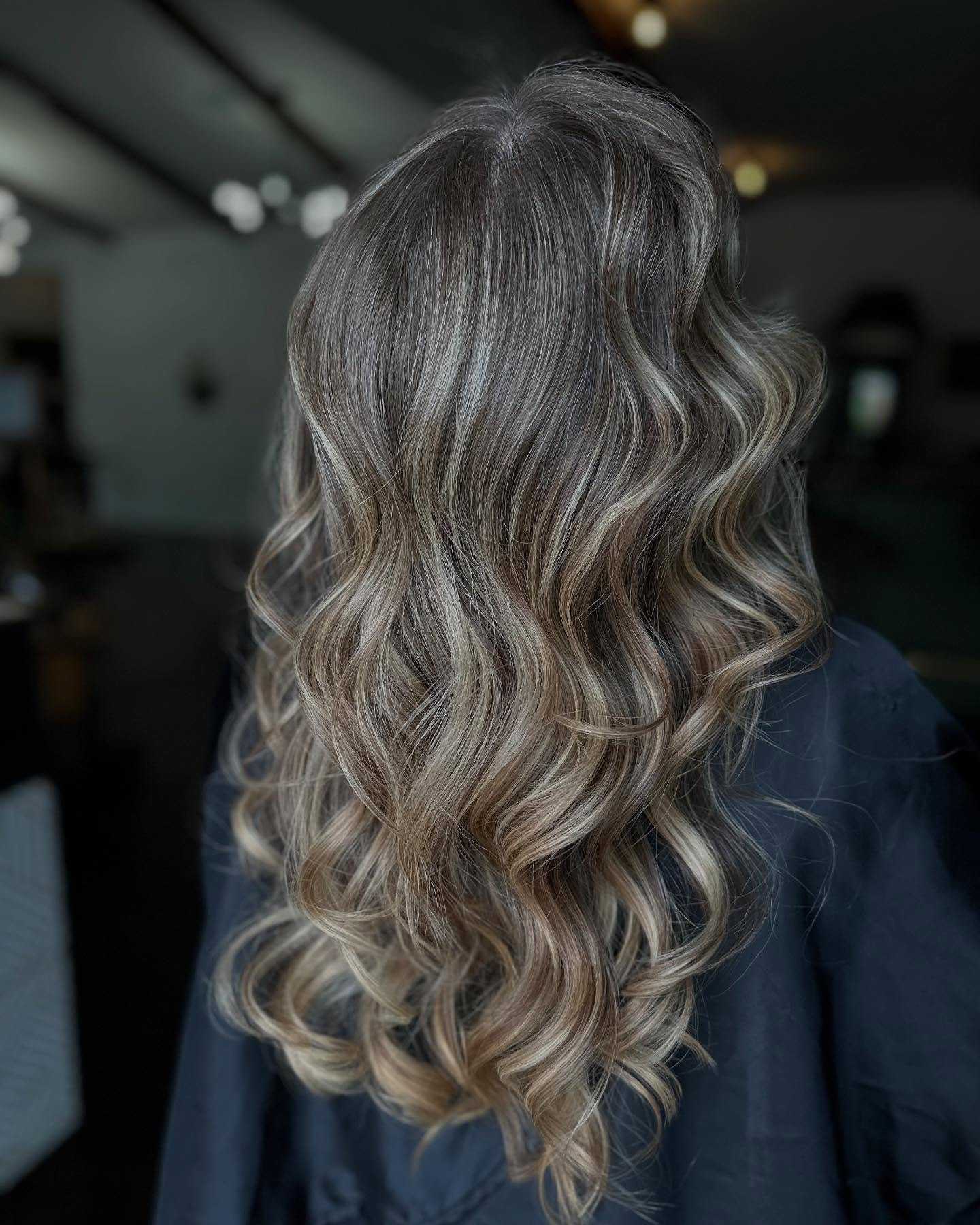 Wavy long hair with soft highlights, back view, in a dimly lit salon.