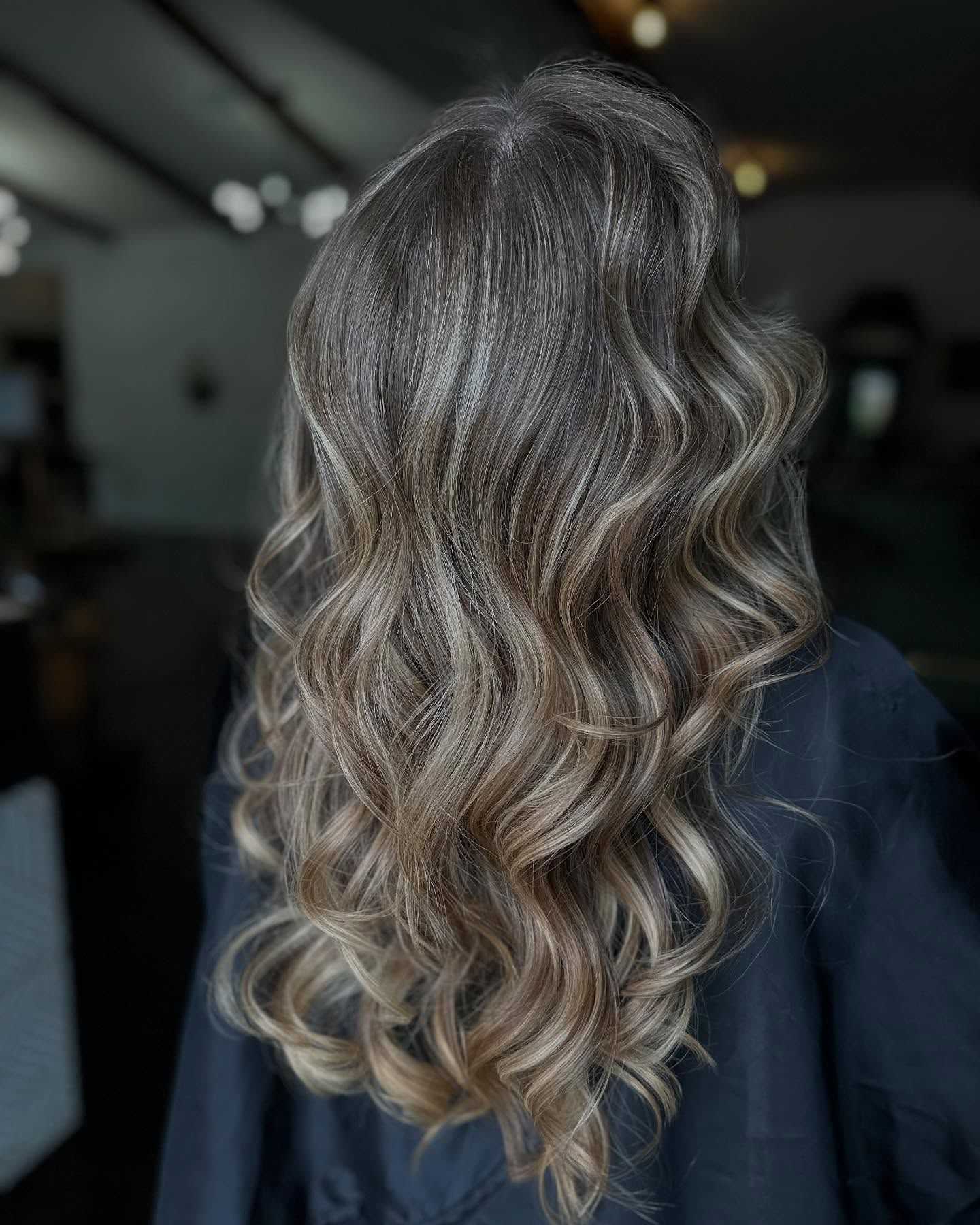 Wavy long hair with soft highlights, back view, in a dimly lit salon.