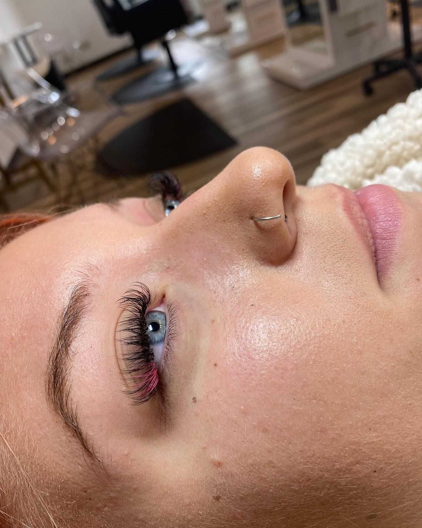 Close-up of a woman's face showing freshly done eyelash extensions in a salon setting.